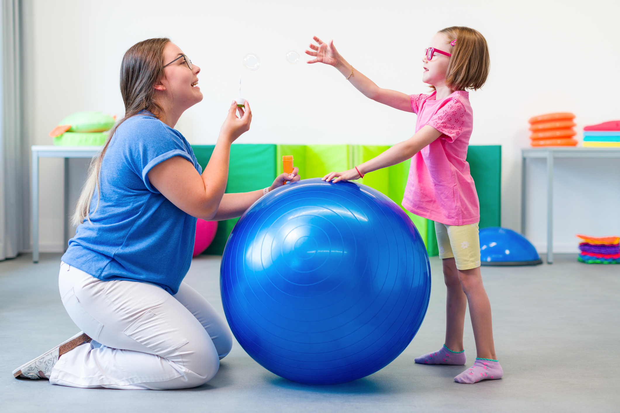 Child with physical disability in bilateral coordination physiotherapy. Child living with cerebral palsy exercising with her therapist during physiotherapy.